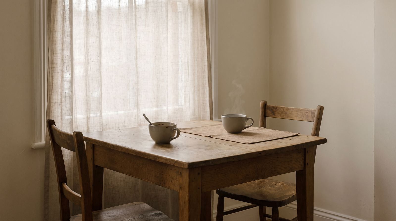 Two cups on a kitchen table, one drunk from and one untouched.