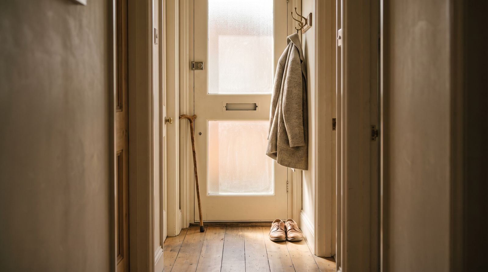 A hallway by a front door, a walking stick against the frame and a coat on a hook.