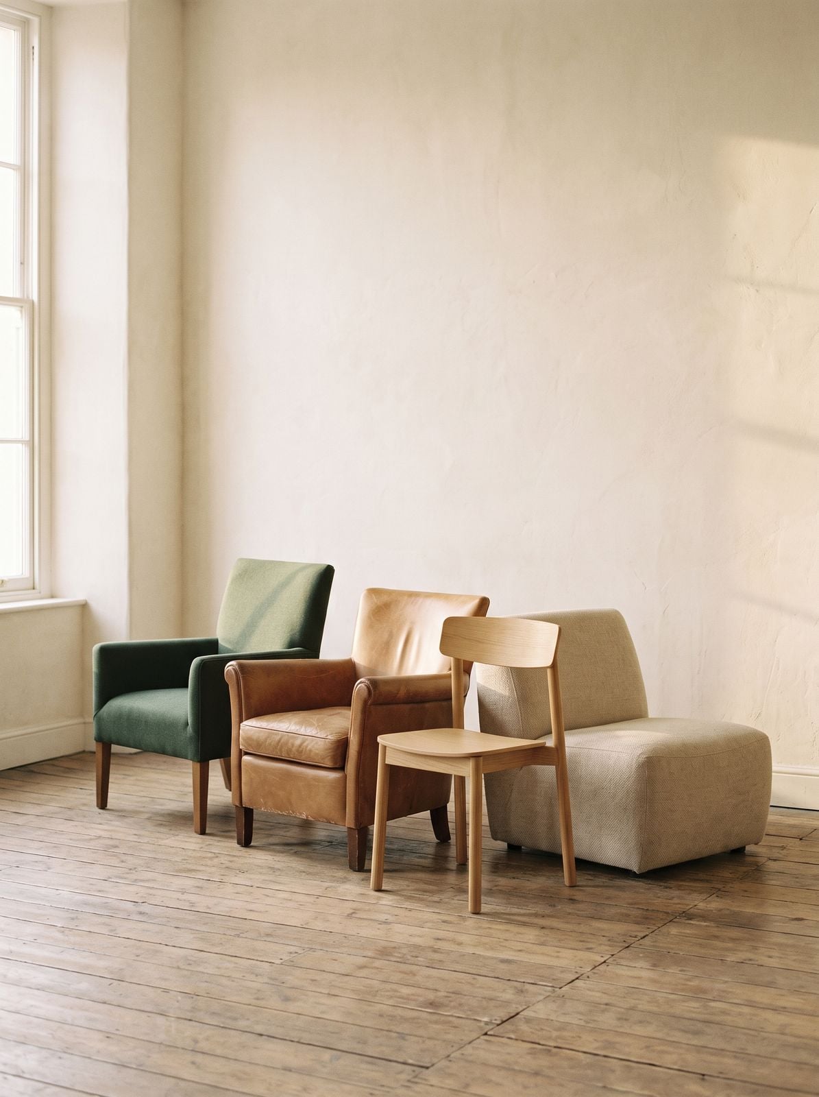 Four different chairs standing together against a plain wall.