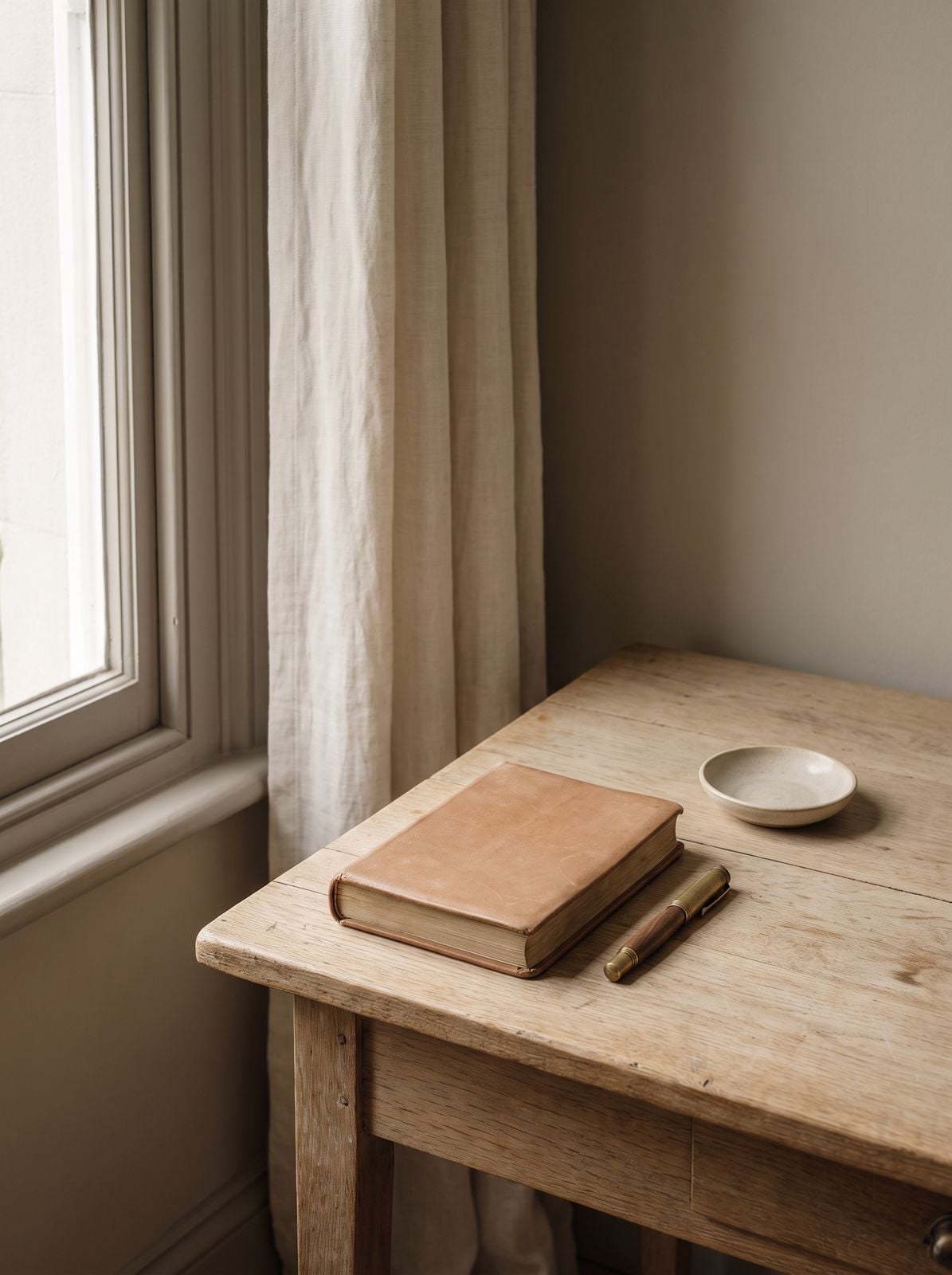 A desk by a window with a closed appointment book and a pen.